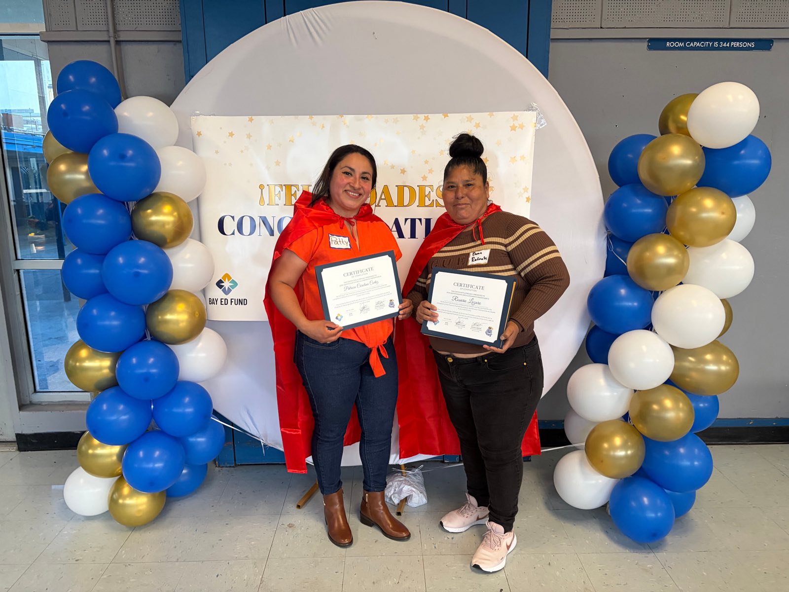 Two Promise Champions parent leaders in red capes holding their certificates of completion